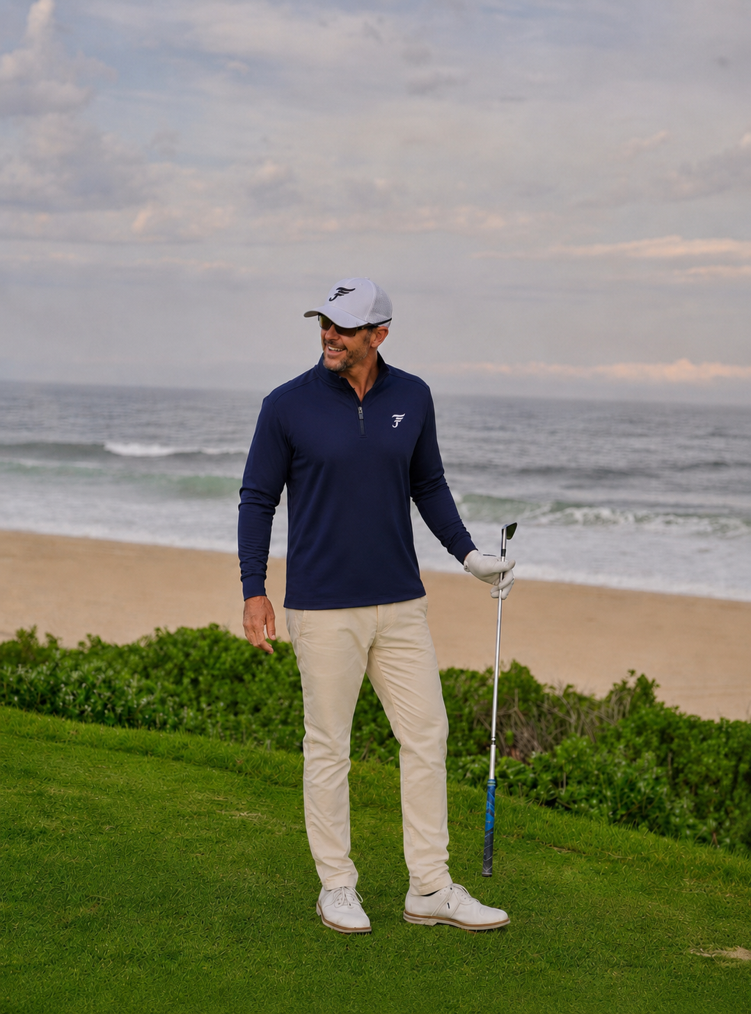 Man in golf attire standing on a golf course with ocean in the background