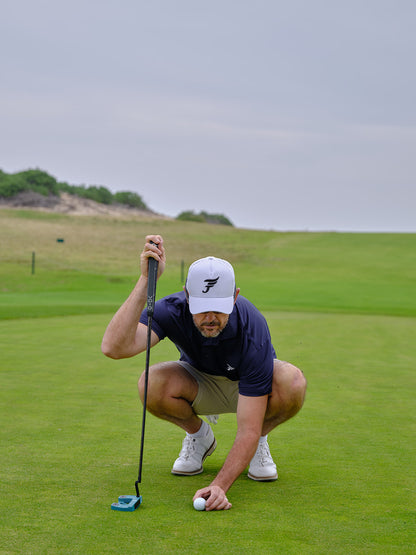 Man on a golf course preparing to putt with a white cap and navy shirt.