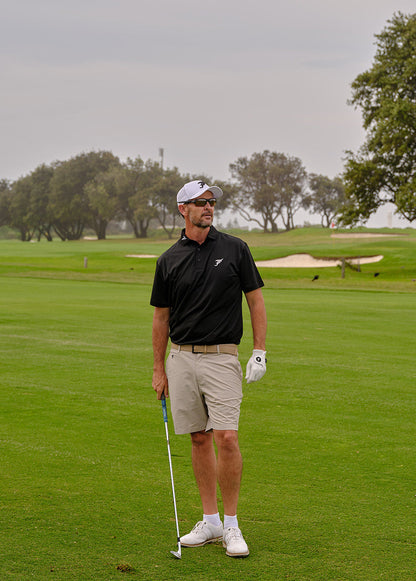 Man on a golf course holding a golf club and ball, with trees and greenery in the background.