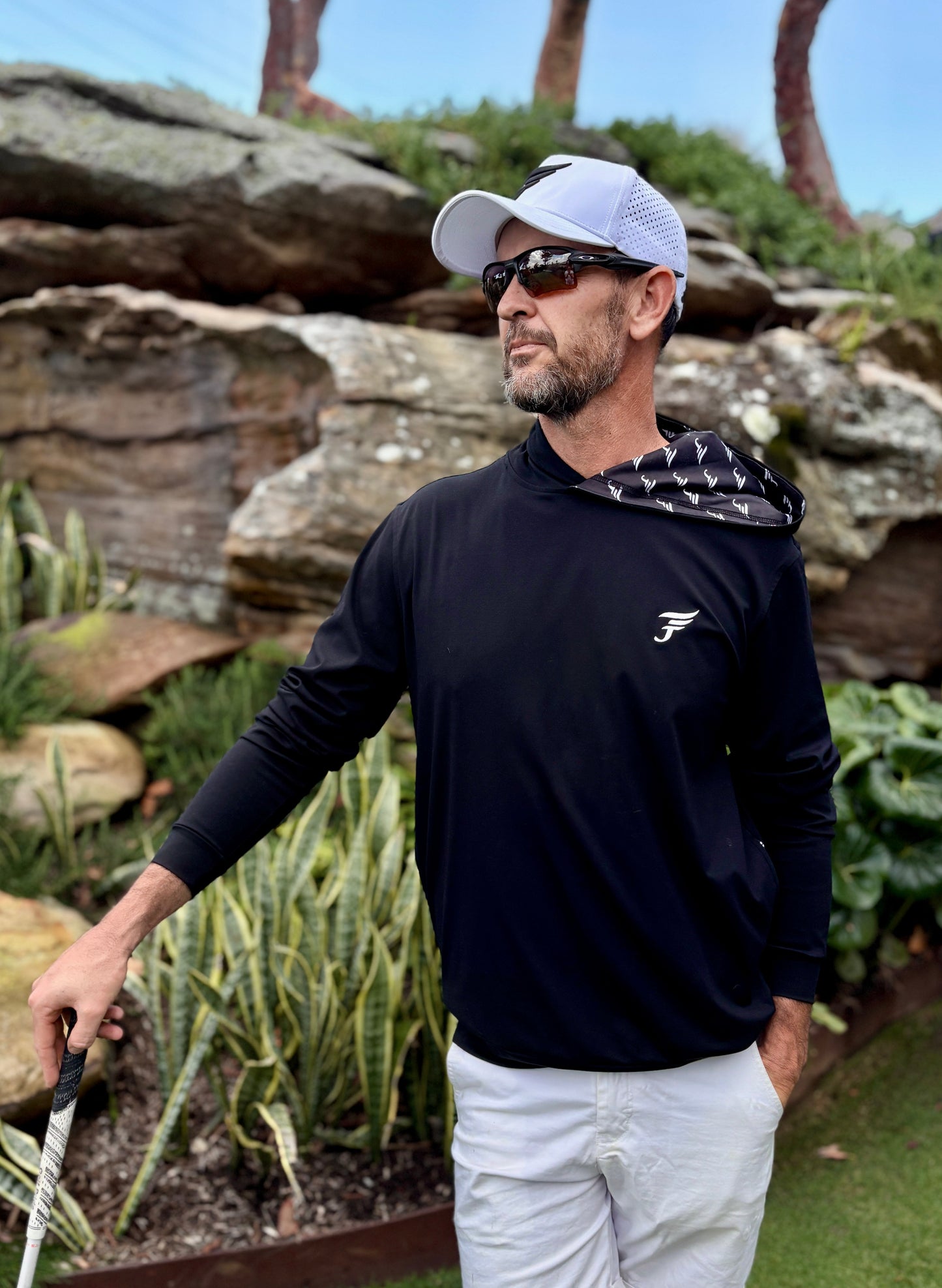 Man in golf attire standing on a golf course with rocks and plants in the background
