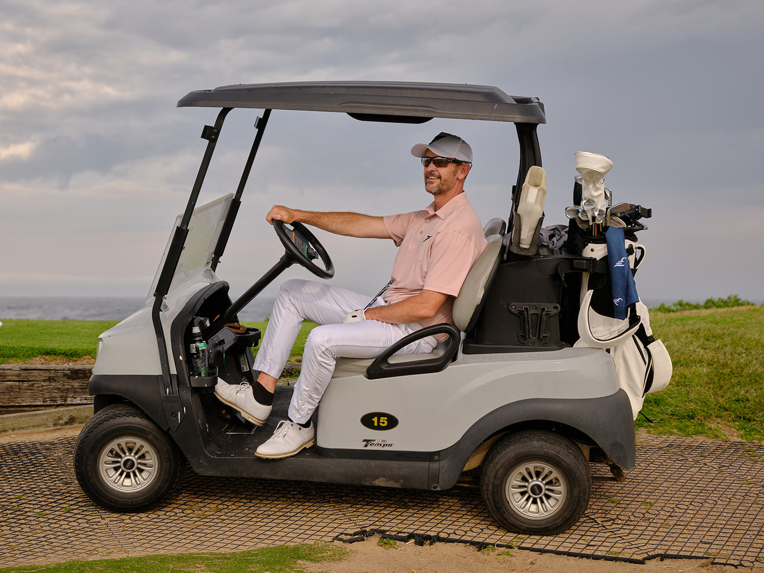 Man driving a golf cart on a golf course with a cloudy sky.